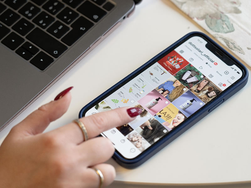 Come nasce un prodotto professionale: mano su smartphone con social media, prodotti Dottsolari, laptop. Focus sui capelli.