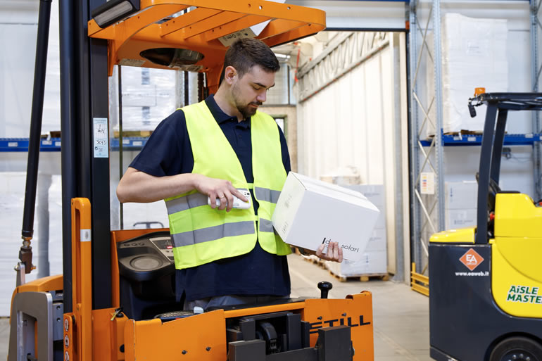 Operaio di magazzino su carrello elevatore che scansiona un pacco. Logistica e spedizioni efficienti con tecnologia avanzata.