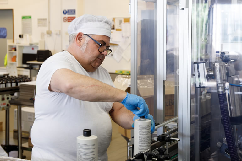 Dott. Solari Marco staff al lavoro: uomo in cuffia e guanti blu controlla flaconi su linea di produzione. Qualità garantita.